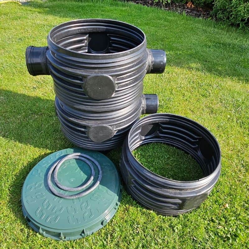 Čierna vlnovcová filtračná šachta STRONG so samostatným nadstavcom položeným na trávniku.